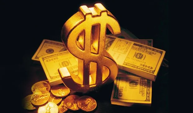 A golden dollar sign stands prominently in the foreground against a dark background, surrounded by a glow that highlights its shape. Scattered around it are several hundred-dollar bills and golden coins, giving an impression of wealth and prosperity. This image symbolizes financial success and could be related to earning revenue through methods other than AdSense in the context of blogging