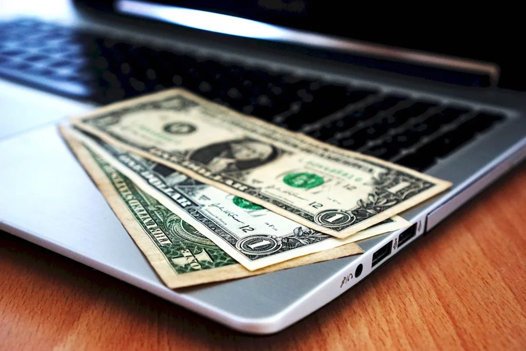 A close-up image of a few U.S. dollar bills placed on the keyboard of an open laptop, symbolizing the concept of online earnings or monetization.