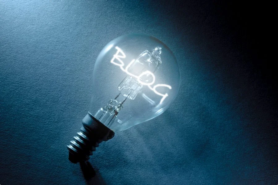 Photo of a lightbulb on a textured dark blue background with the word 'BLOG' filament illuminated from within, suggesting the concept of blogging as a bright idea or a source of inspiration. The image could be a metaphor for the illumination and potential of earning through advertising on a blog or website.