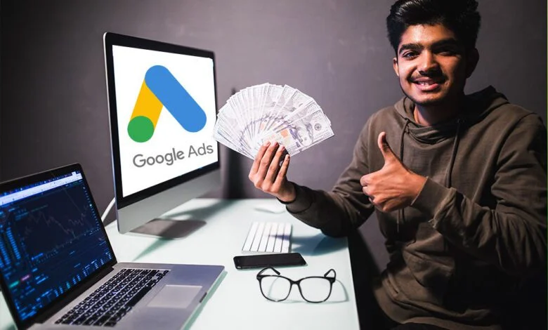 A young person gives a thumbs-up while holding a fan of banknotes, with a laptop showing financial data on the screen to the left, and a monitor displaying the Google Ads logo to the right. The setting suggests successful monetization, likely through digital advertising platforms like Google Ads