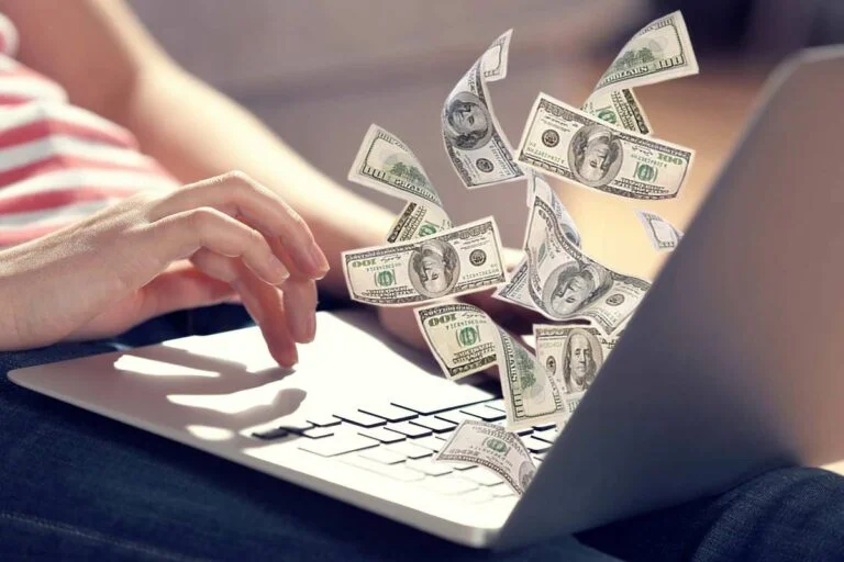 A person is using a laptop, and illustrated money bills are emerging from the screen, symbolizing the earning or monetization of online content