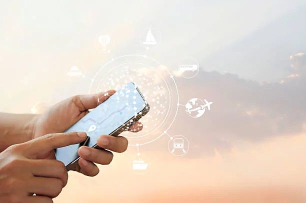 A pair of hands holding a smartphone with a digital interface superimposed over a soft-focus background suggestive of a sunrise or sunset. The screen displays various icons and symbols representing connectivity and technology services, such as GPS location, transportation, and communication networks, symbolizing the integration of advanced technology into everyday life.
