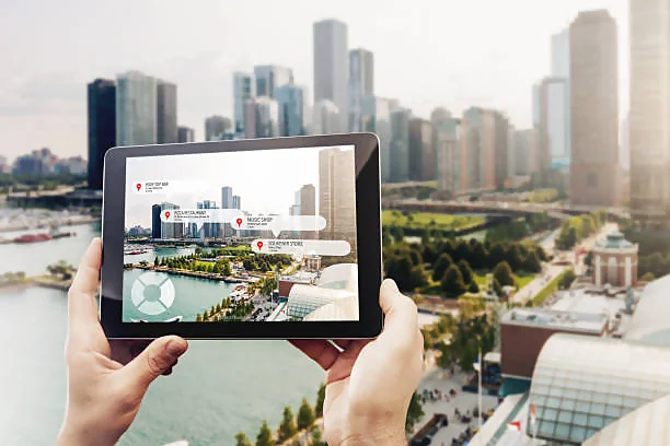 Hands holding a tablet with an augmented reality (AR) view of a cityscape. The tablet screen overlays interactive tags with information bubbles over specific buildings, suggesting points of interest or locations within the urban environment. The backdrop features a real-life city skyline, blending the digital enhancements on the tablet with the physical world, symbolizing the fusion of modern technology and daily life exploration