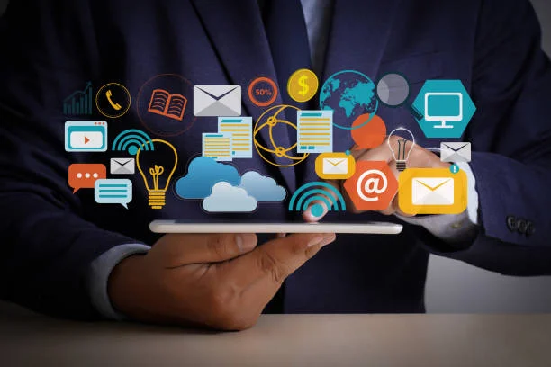 A person in a dark suit holds a tablet with various colorful icons floating above it, symbolizing different digital services and concepts such as email, cloud computing, networking, global connectivity, finance, time management, and multimedia.